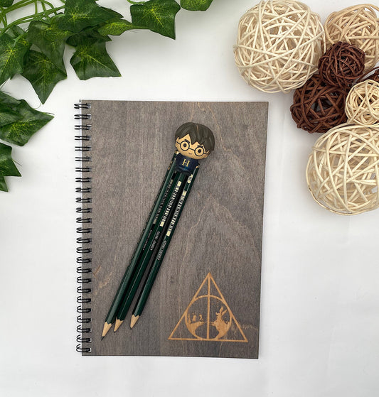 Notebook with pencils and a pen holder on a white surface with decorative elements.