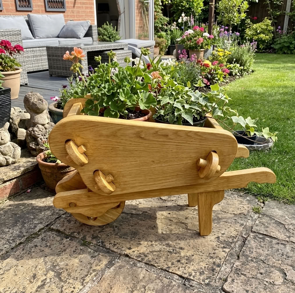 A small wooden garden wheelbarrow planter made of natural pine with a light oak wood stain, filled with potted green plants, set on a stone patio in a backyard garden.