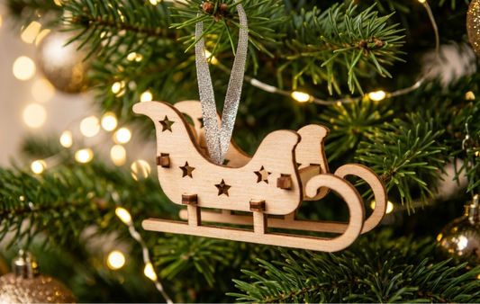 A wooden sleigh Christmas ornament hanging from a green Christmas tree with warm white string lights and gold bokeh background lights.