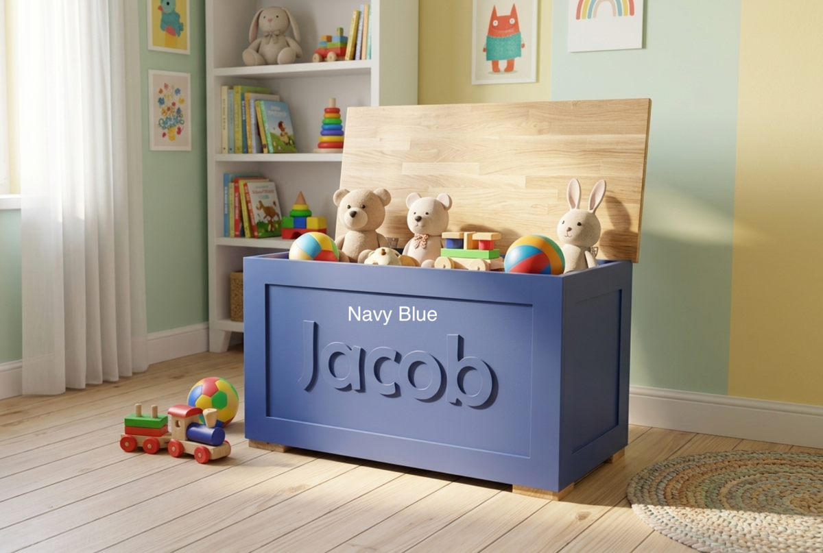 A personalised navy blue wooden toy storage box with the name 'Jacob' embossed on the front and an oak lid, styled in a child's room with toys and a wooden bench behind it.