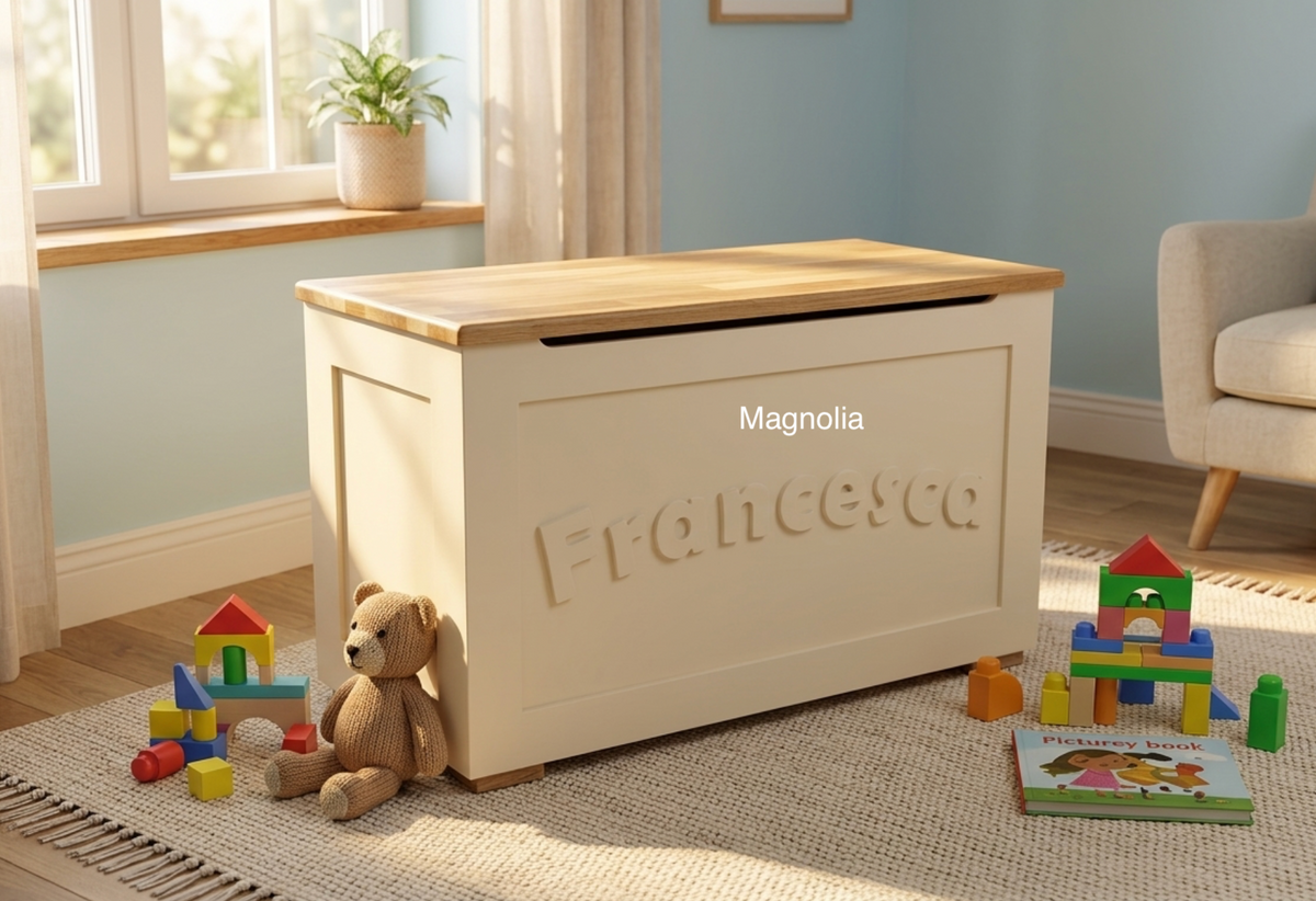 A cream-coloured magnolia wooden toy storage chest with an oak wood top, personalised with the name 'Francesca' on the front, styled in a child's room with toys and a teddy bear.